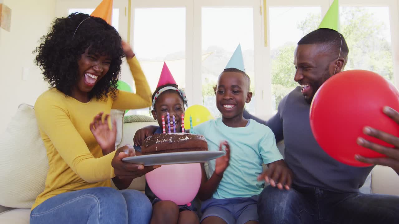 Bambino afroamericano che soffia le candeline sulla torta e festeggia il compleanno con la famiglia a casa.