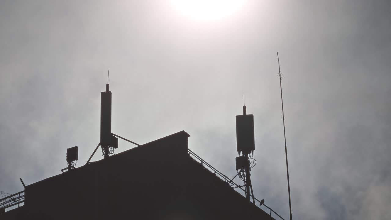 Silhouette di antenne di comunicazione su tetto contro cielo luminoso