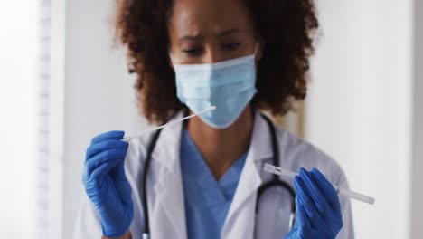 Mixed-race-female-doctor-wearing-mask-inspecting-patient-swab-test