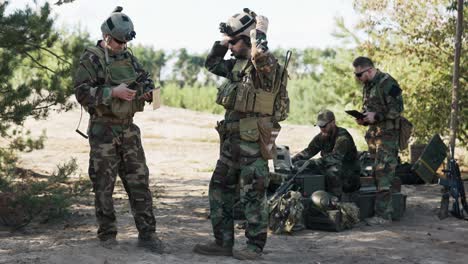 un grupo de soldados se está preparando para ir en una patrulla en el campo, establecen una estrategia, una ubicación, siguen un mapa en una computadora, una tableta, un líder de tropas se pone un casco
