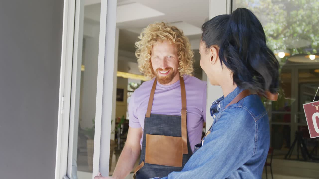 Portrait of happy diverse male and female baristas in aprons outside their coffee shop