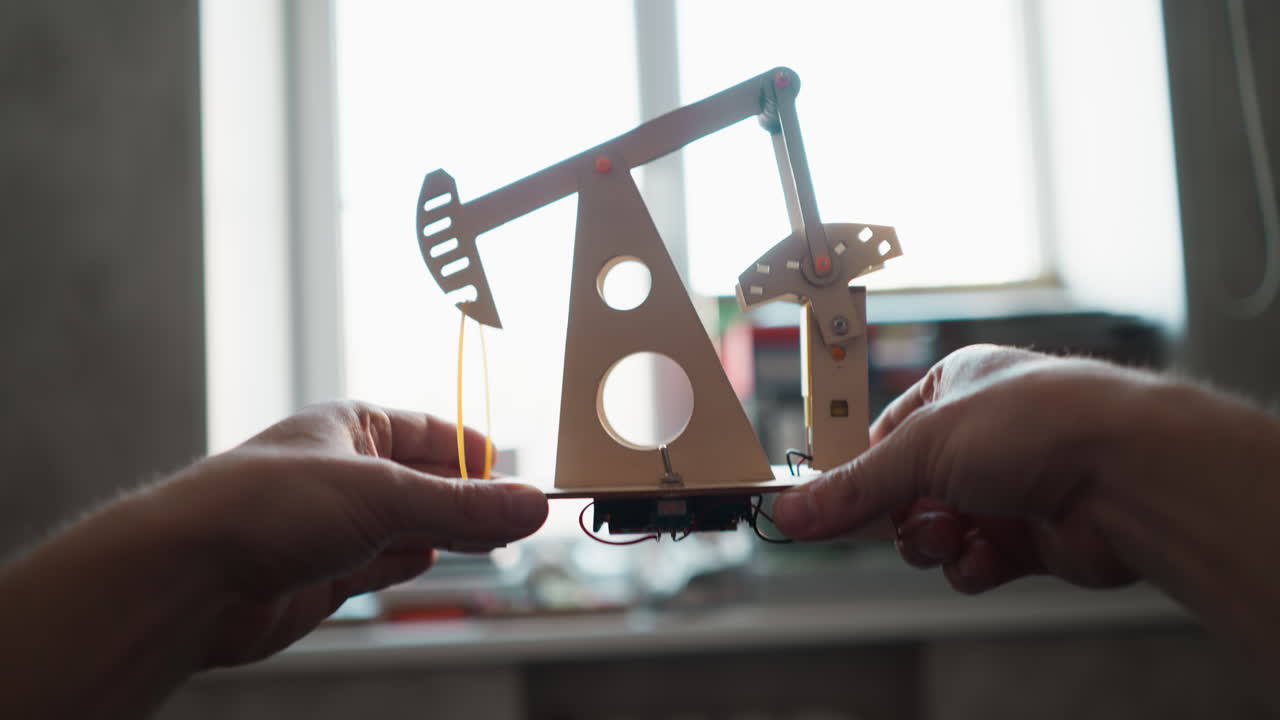 전자 장치를 확인하는 작업 데스크에서 유동화 된 오일 프 잭 모델을 창문 수준으로 들어 올리는 사람의 pov