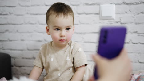 sweet caucasian toddler looking at phone shown by parent. lovely baby is interested, smiles and says something.