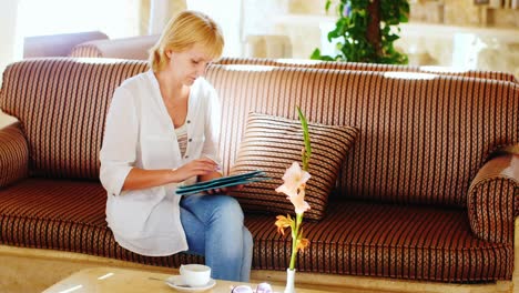 Frau-Im-Sommerhemd-Benutzt-Ein-Tablet-In-Der-Hotellobby