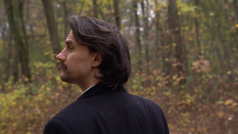 man with dark hair and mustache walking in the forest, looking around