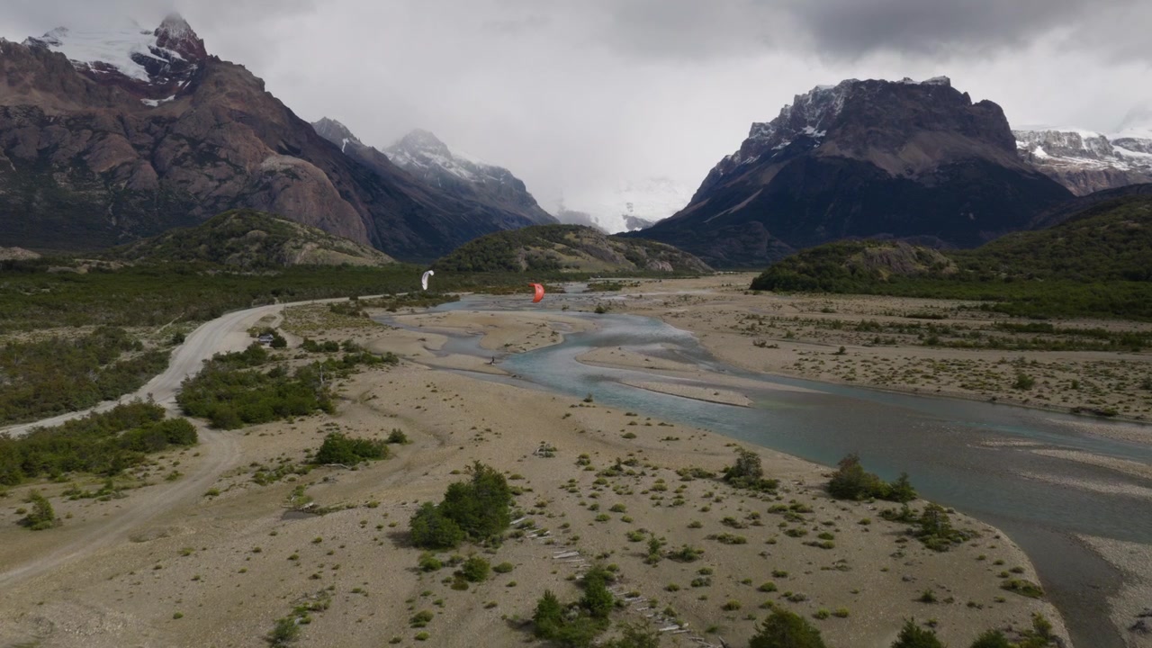 Kitesurfer si muovono attraverso i canali intrecciati del Río de las Vueltas vicino a El Chaltén, Santa Cruz, Argentina, circondati da valli glaciali, Ande aspre e steppa patagonica, ripresa con drone in avvicinamento