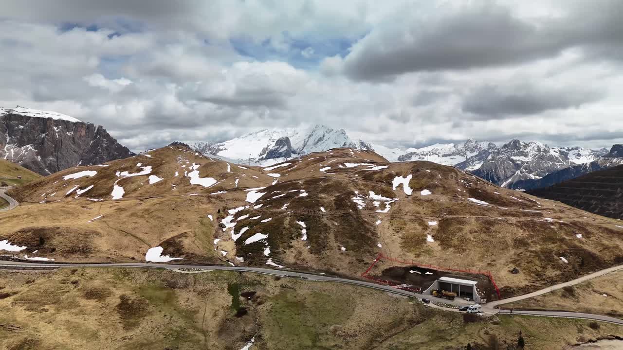 Drone turn following winding road on Sella pass in Dolomites, with high peaks and dramatic sky, Italy travel