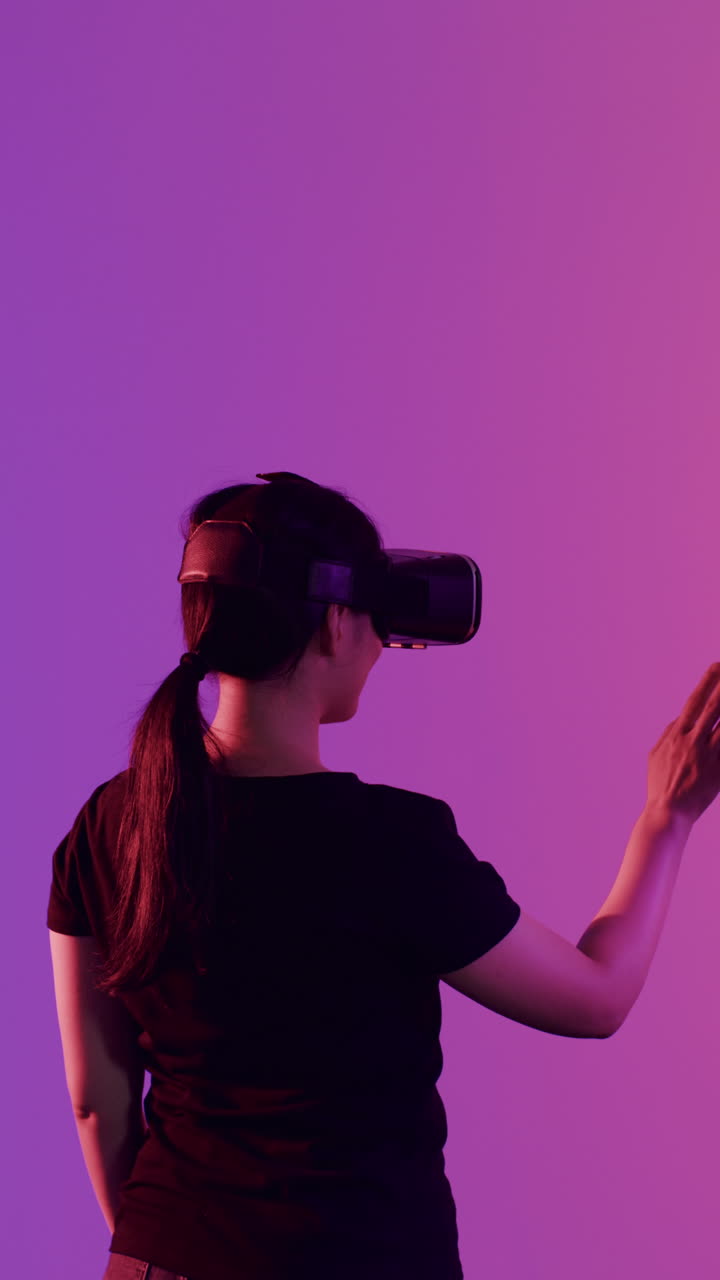 Vertical video of asian woman and woman using vr headsets on purple background, slow motion