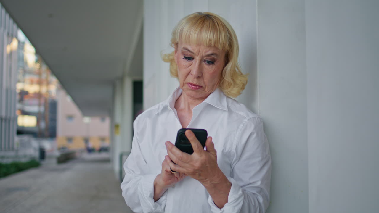 Eldre dame bruker app på smarttelefon mens hun venter på taxi på gaten, nærbilde.
