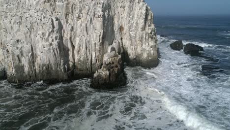 foamy waves crashing against rock formation, piedra de la piramide in chile - aerial drone shot