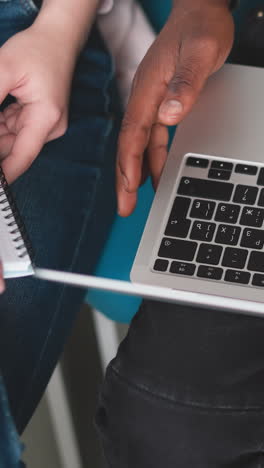 black man with laptop on lap indoors closeup. african american employee uses modern computer sitting with colleague in office. guy works online via device