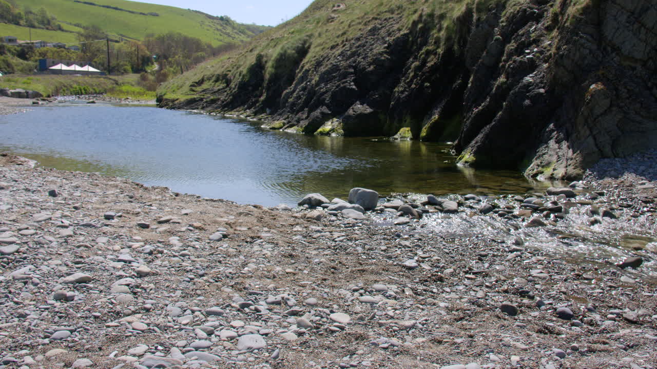 Extra wide shot of the river Tydu Forming a pond and flowing over pebbles and rocks on at Cwmtydu beach