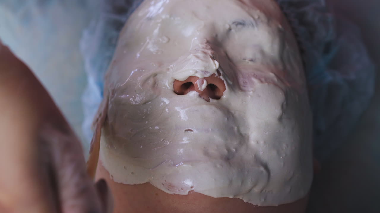 el cosmetólogo cubre el rostro de la mujer con una máscara de alginato en la clínica