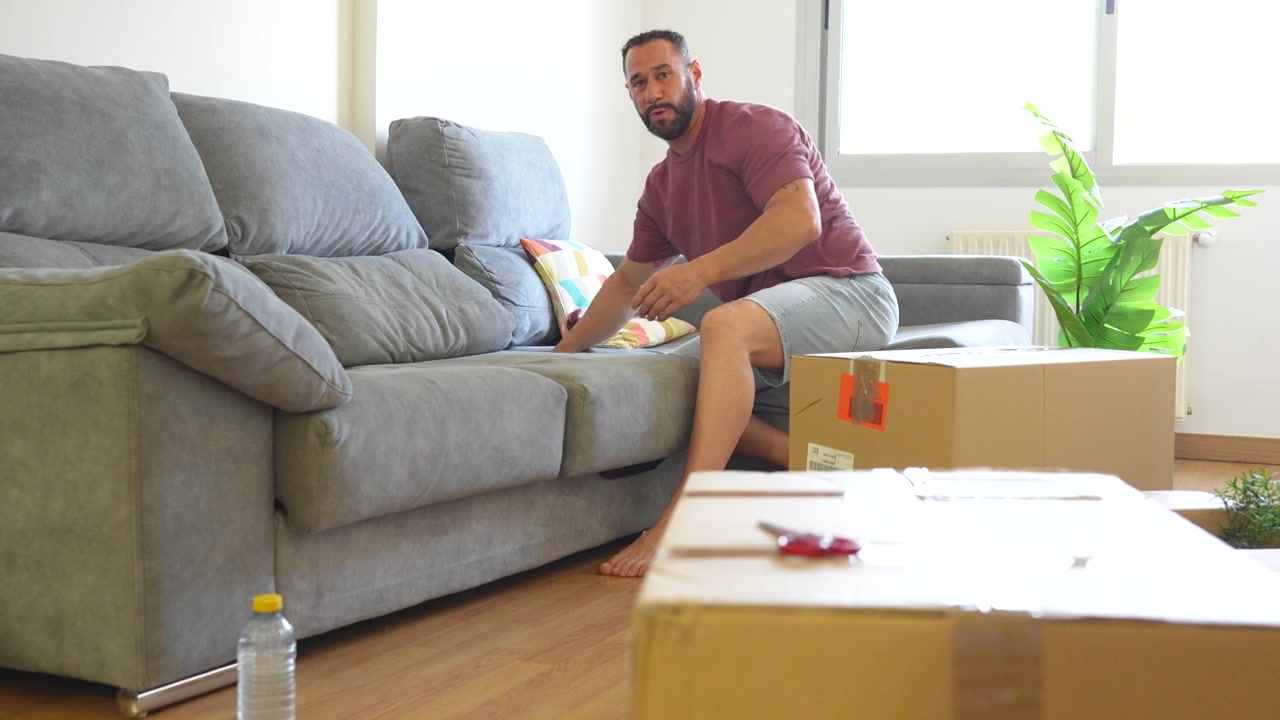 Middle aged man assembling a sofa in his new home surrounded by cardboard boxes during a move