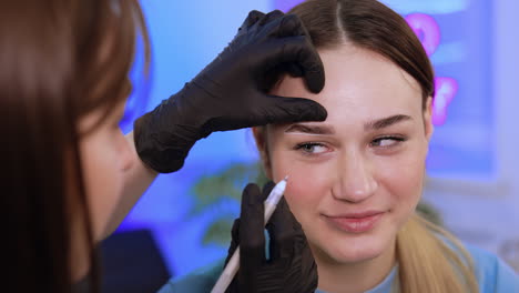 salon brow master applying white marks around girl's eyebrows. preparatory process for eyebrow make up. close up.