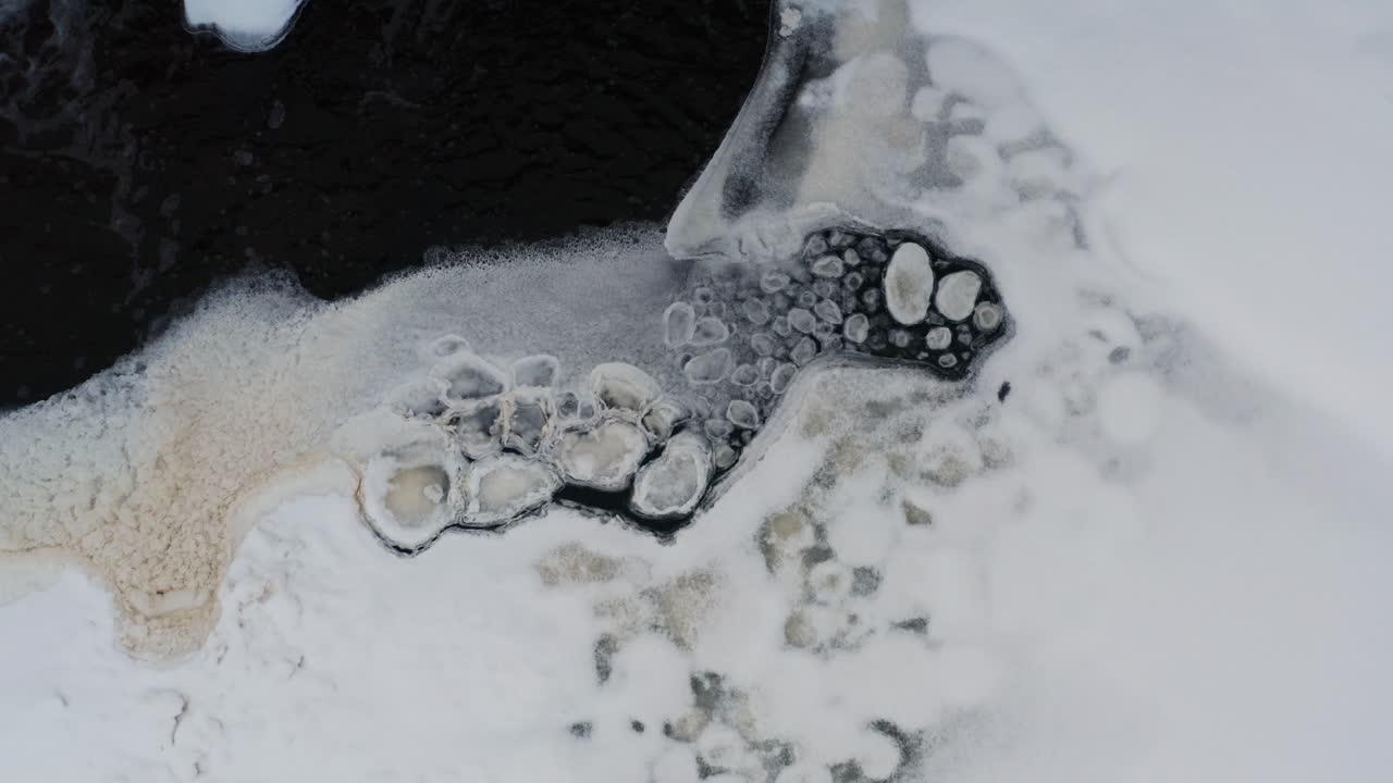 Aerial descend over ice shape and foam formations near pond ice sheet