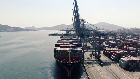 aerial views of a busy shipping dock with containers and a cargo ship unloading at a port during daytime, illustrating maritime trade and logistics operations