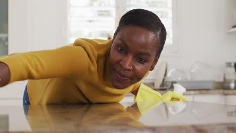 Happy-african-american-female-cleaning-countertop-in-kitchen