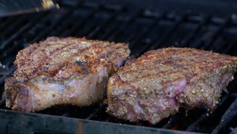 un par de pinzas para carne colocan un jugoso filete de costilla casi cocido en una parrilla y lo deslizan un poco
