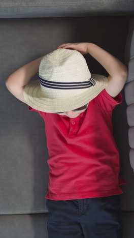 stylish small boy puts hands behind head lying on sofa near suitcase. toddler in sunglasses and hat relaxes in hotel room upper close view