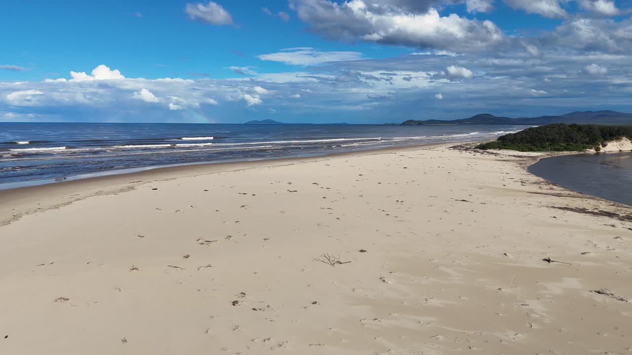 Aerial drone glides over wide, empty sandy beach with seaweed at Nambucca Heads, Australia