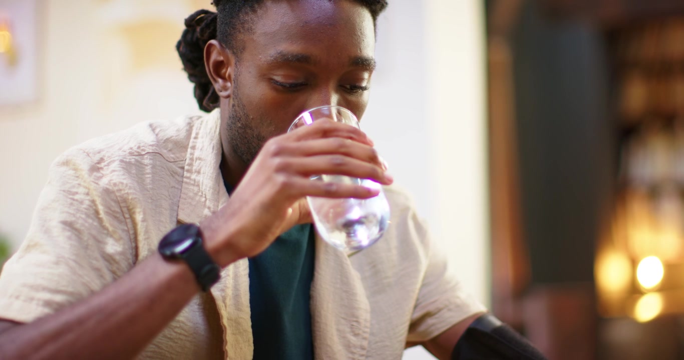 African American man pressing BP button to check BP, adjusting cuff, drinking water at table