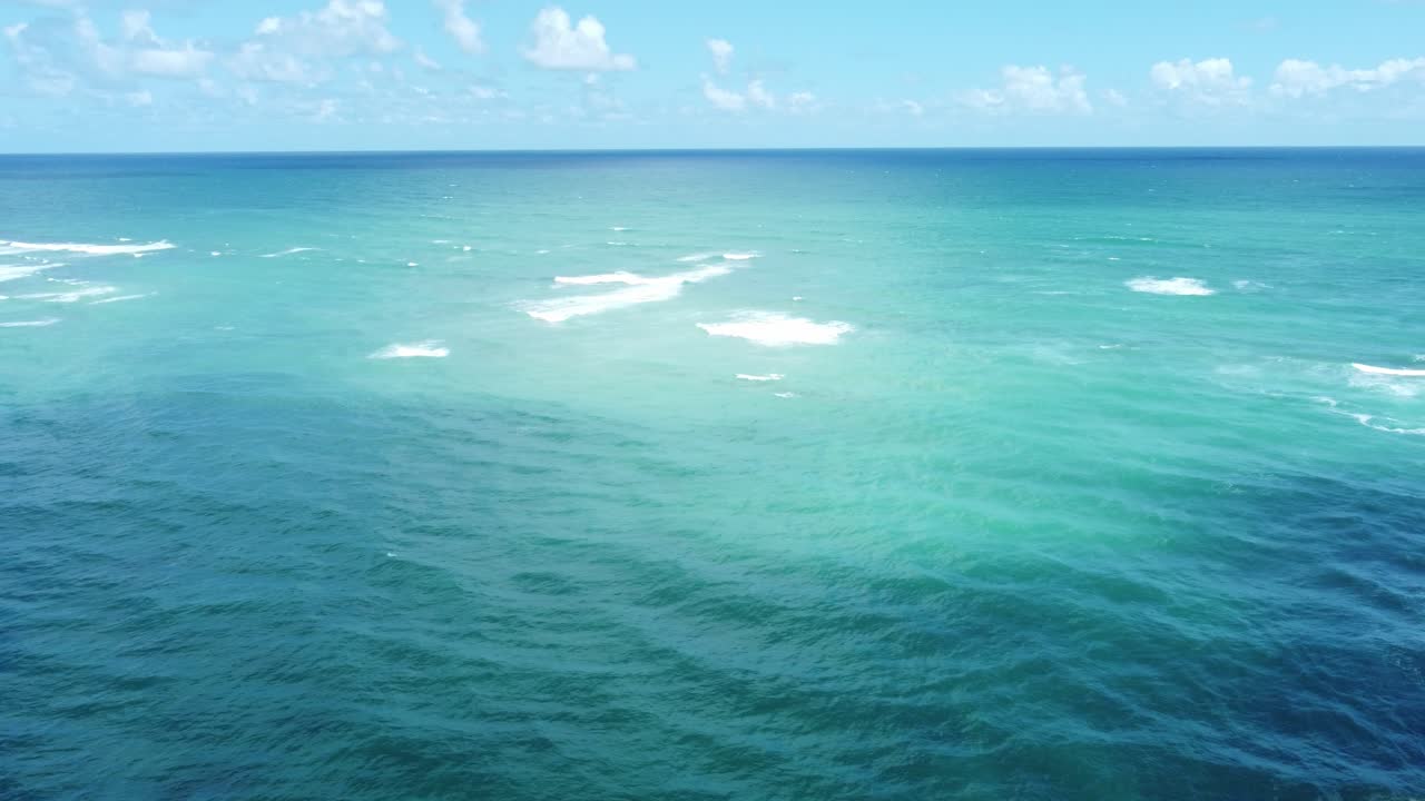 오아후 바다의 드론의 공중 풍경은 태평양 물의 놀라운 깨함을 보여줍니다. 파도가 부드럽게 해변을 향해 굴러가고 활기찬 파란색 색조가 지평선까지 어 있습니다.