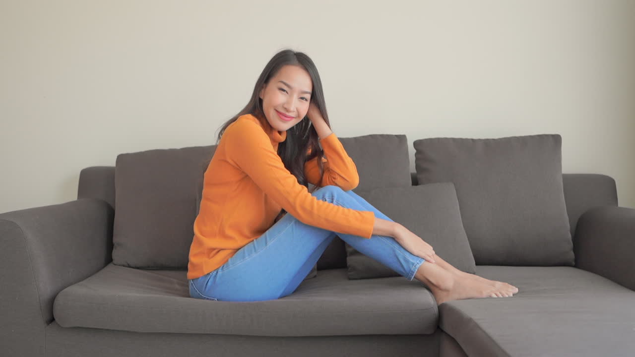 Cheerful pretty Asian girl on couch smiles posing looking at camera