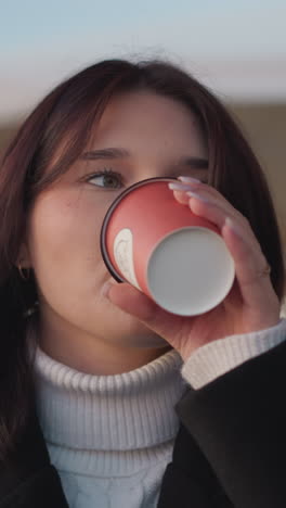 원격 노동자가 컵을 내려놓기 전에 커피를 부드럽게 마시고, 야외에서 평화로운 순간을 즐기고, 흐릿한 마당과 배경에 부드러운 바람