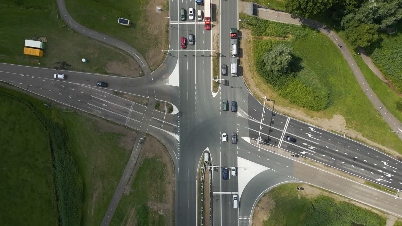 Directly overhead drone shot of Dutch multilane road junction with cars and bike lanes in green surroundings