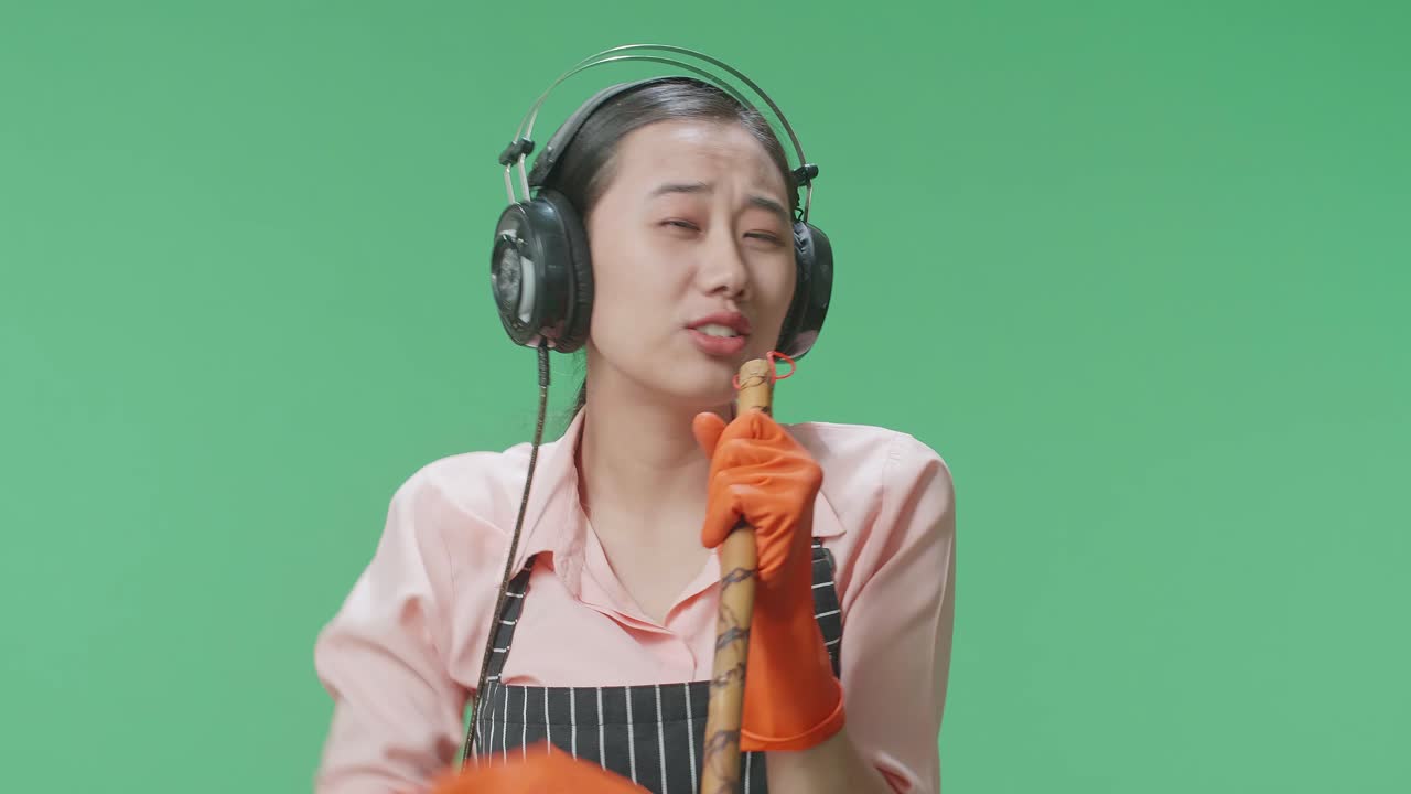 초록색 스크린 스튜디오에 서서 헤드폰을 착용하고 는 자루에 노래하는 아시안 여성 집주인의 클로즈업