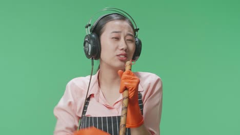 초록색 스크린 스튜디오에 서서 헤드폰을 착용하고 는 자루에 노래하는 아시안 여성 집주인의 클로즈업