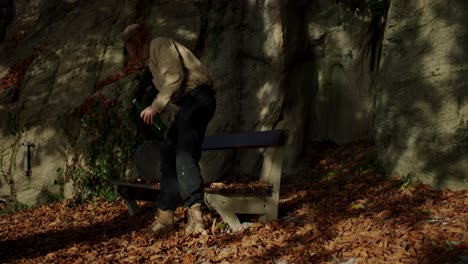 hiker walking on autumn leaves to sit on bench and drink water after long journey