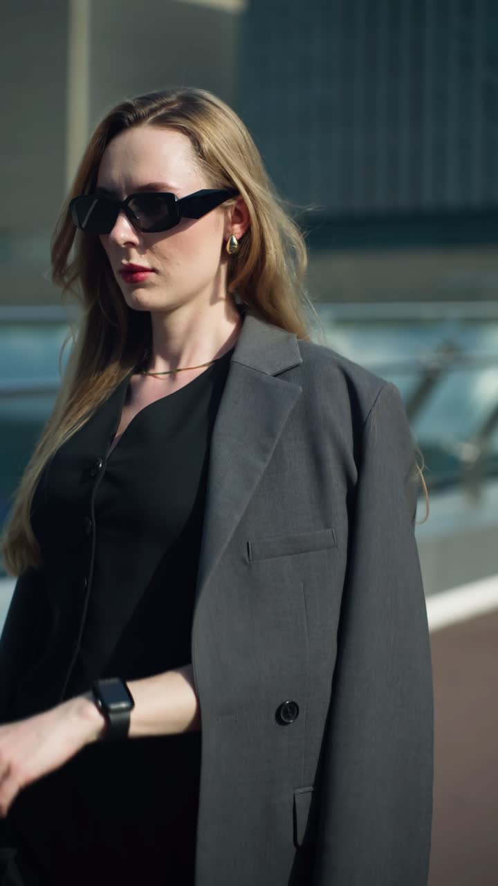 A busy professional woman in a stylish suit and sunglasses checks the time on her smartwatch, managing her schedule while on the go in the city - tracking slow motion