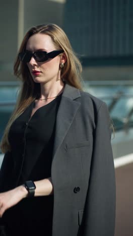 a busy professional woman in a stylish suit and sunglasses checks the time on her smartwatch, managing her schedule while on the go in the city - tracking slow motion
