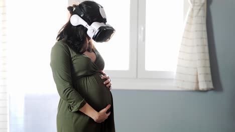 Young-pregnant-female-in-VR-goggles-standing-near-window-and-touching-tummy