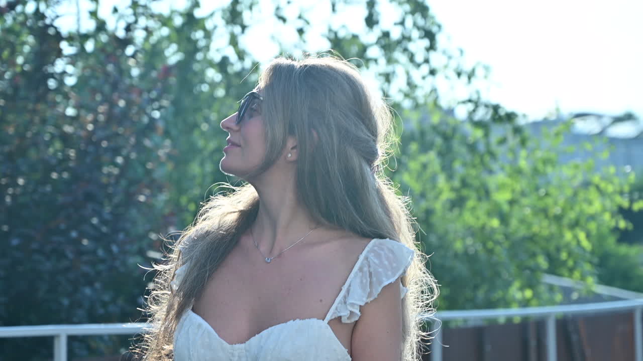 Brunette woman in white dress standing on a roof near trees