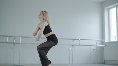 fit girl in black clothes performing contemporary. female dancer shows flowing motions, body and hands waves at white room. modern ballet dance choreography. young woman is moving smoothly