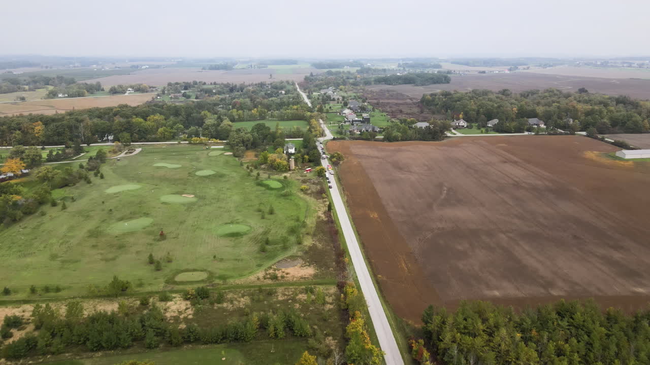 Aerial View of Countryside Nature Landscape at Cloudy Day in Autumn Season, Road Through Green Golf Course Field and Vast Agricultural Lands, Stationary Vehicles at Roadside, Skyline in Horizon