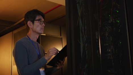 Asian-male-it-technician-using-tablet-checking-computer-server