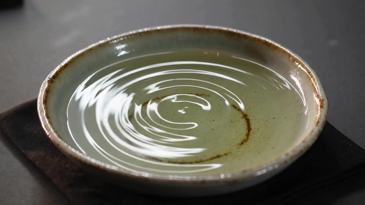 Making circular ripples, liquid in pale bowl on counter reacting to droplet, revealing ring residue