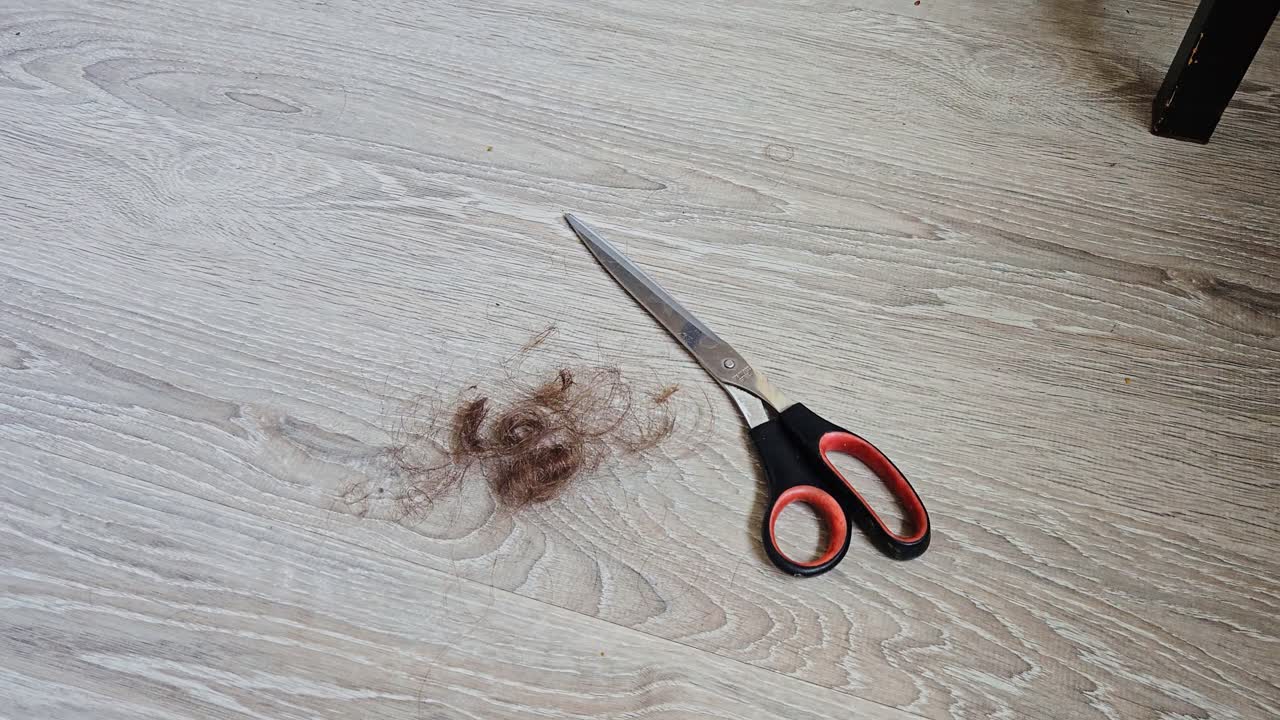 Zooming slow motion reveals freshly cut hair beside scissors on wooden surface
