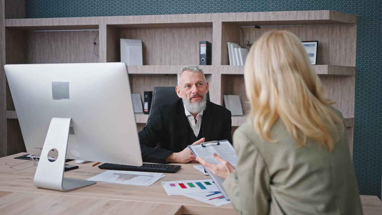 Business routine. Senior man ceo listening to woman manager at office, lady showing notepad, discussing work, zoom in