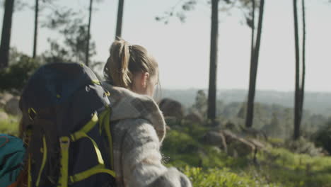 two female friends with backpacks hiking together in the forest on a sunny day