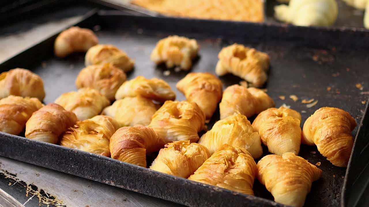 A high angle shot of numerous flaky croissants baking on a rustic metal tray
