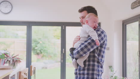 Father-holding-and-comforting-crying-baby-son-carrying-him-around-room-at-home--shot-in-slow-motion