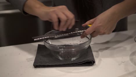 A-young-girl-grates-chocolate-into-a-bowl-for-melting-while-making-millionaire-shortbread-cookies-while-wearing-safety-gloves-2