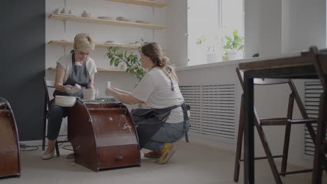 woman master transfers knowledge to an elderly woman working on a potter's wheel and making a mug of ceramics in her workshop in slow motion