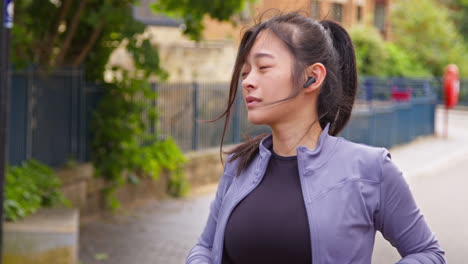 mujer con auriculares inalámbricos estirándose antes de hacer ejercicio corriendo por la calle urbana