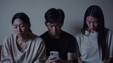 젊은 친구들은 어두운 방에서 스마트폰 스크린을 둘러싸고 긴장하며, 불확실한 정보를 불안하게 처리하는 동안 깊은 우려와 디지털 시대의 감정적 연결을 공유합니다.